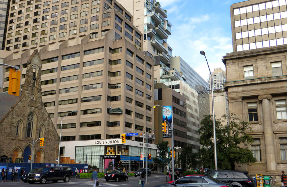 Bloor Street, com igreja, vários carros, pedestres e lojas de luxo.