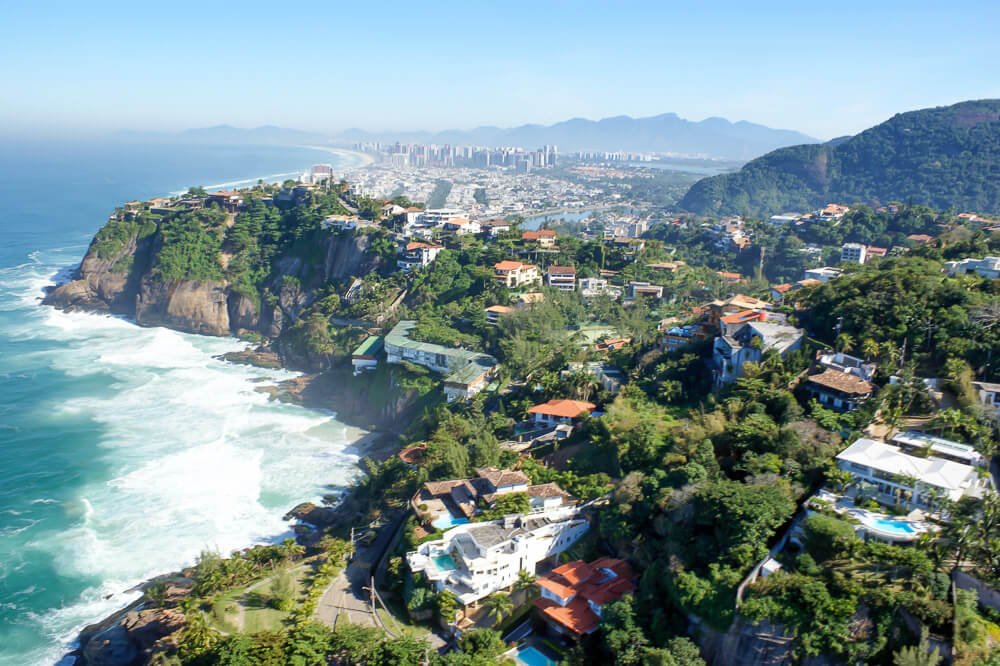 Região da Praia de Joatinga vista de cima, com muitas ondas, muitas árvores e algumas casas à beira-mar.
