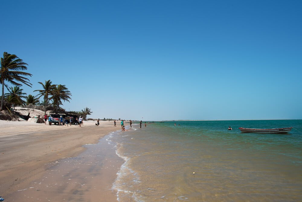 Praia de Atins, com águas verdes, banhistas e coqueirais.