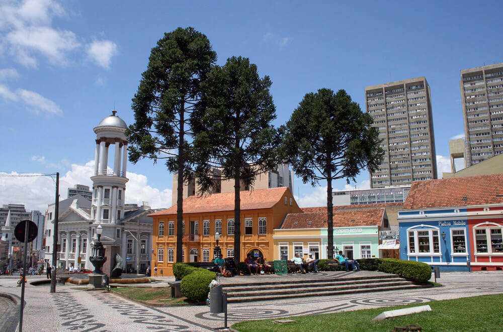 Igreja, prédios históricos, estabelecimentos comerciais e algumas árvores compõem o cenário da Praça Garibaldi, no Centro Histórico de Curitiba.