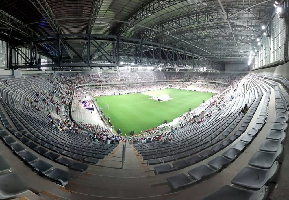 Visão interna do estádio de futebol Arena da Baixada iluminado à noite.