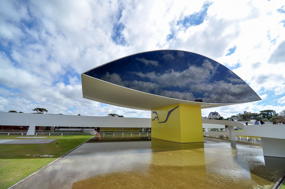 Museu Oscar Niemeyer refletindo as nuvens em um dia iluminado.