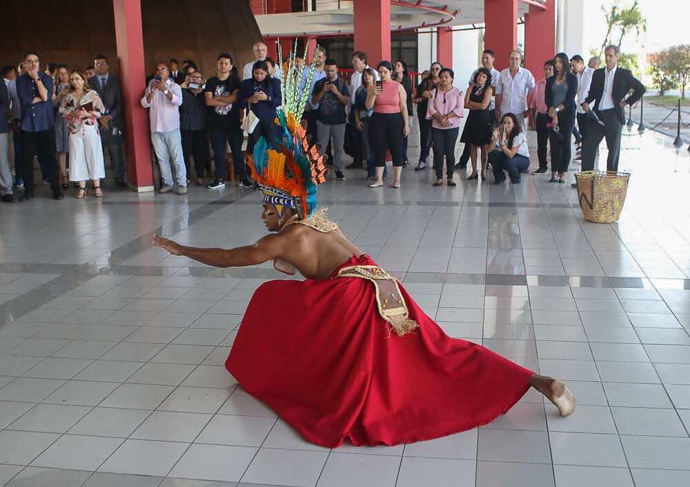 Um homem com vestimentas indígenas coloridas fazendo uma apresentação de dança com elementos indígenas amazônicos no CCPA.