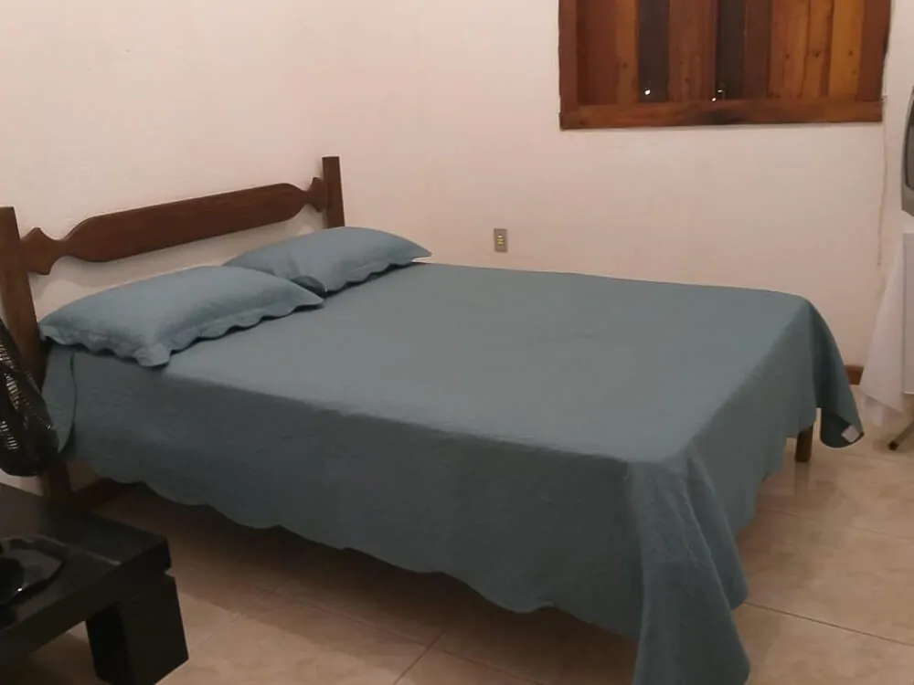 Quarto da pousada Chalés Mucios, com cama de casal e janela de madeira.