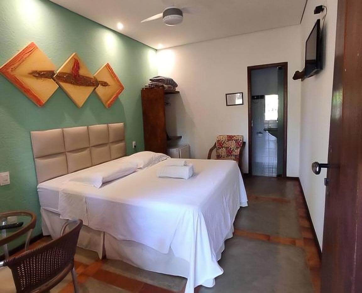 Quarto da Pousada Banana Cipó, com cama de casal, mesa e cadeira, banheiro e TV.