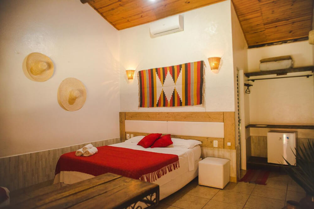 Quarto da Pousada Cipó Prata, com cama, frigobar e aparelho de ar-condicionar.