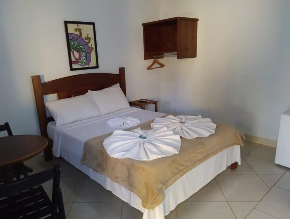 Quarto da Pousada Licuri com cama de casal, mesa com cadeiras e um cabideiro.