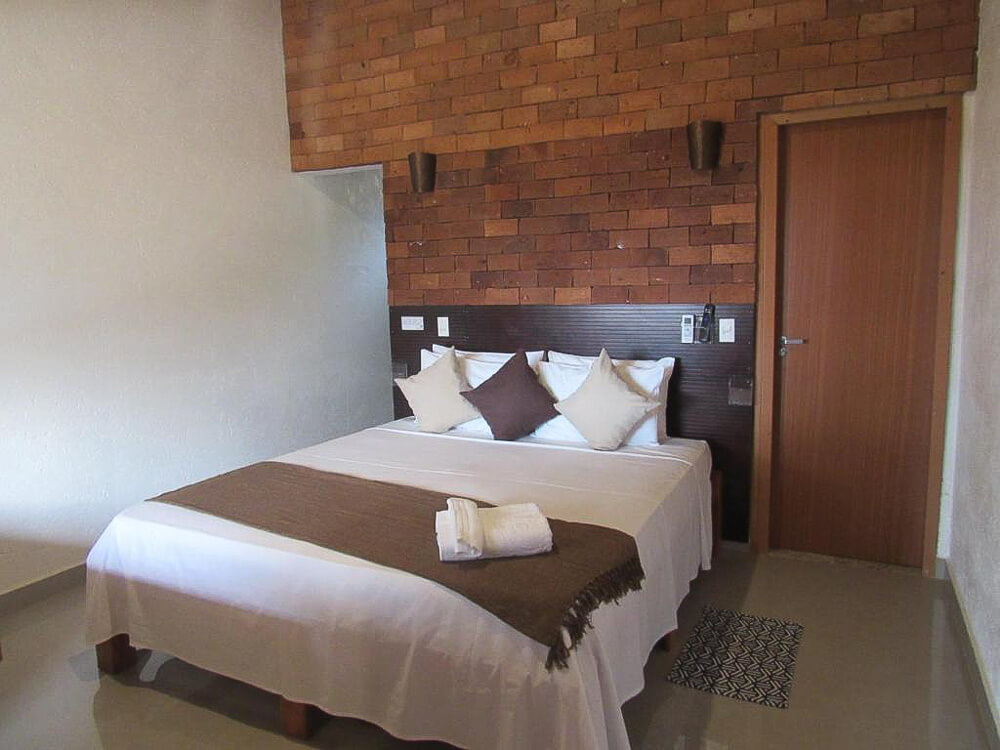 Quarto da Pousada Meraki, com cama de casal e parede tijolos marrons.