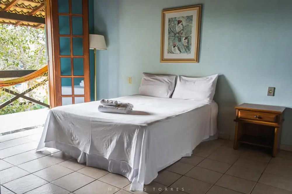 Quarto da Pousada Recanto da Serra, com cama de casal e varanda com vista para a natureza.