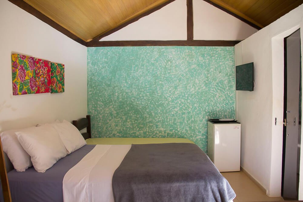 Quarto da Vila Flores Pousada, com uma cama de casal, uma cama de solteiro, TV, frigobar e teto de madeira.