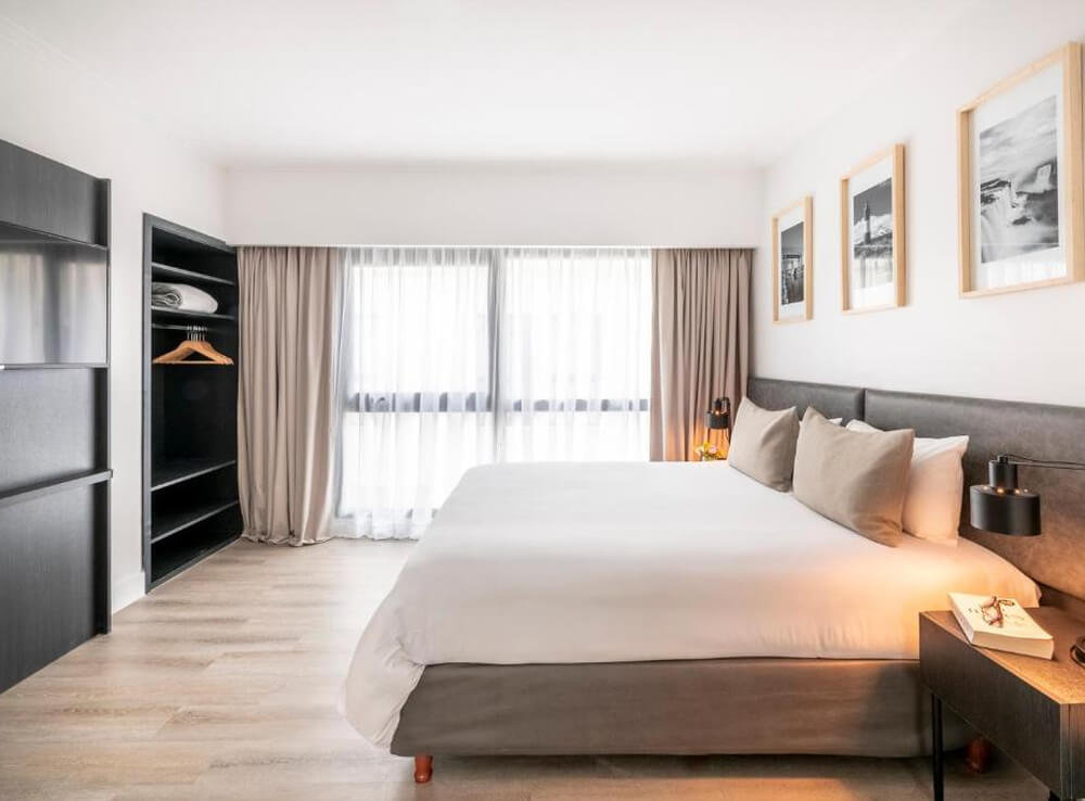 Quarto do hotel Efe Hotel & Cowork, com cama de casal, TV, guarda-roupa e janela grande.