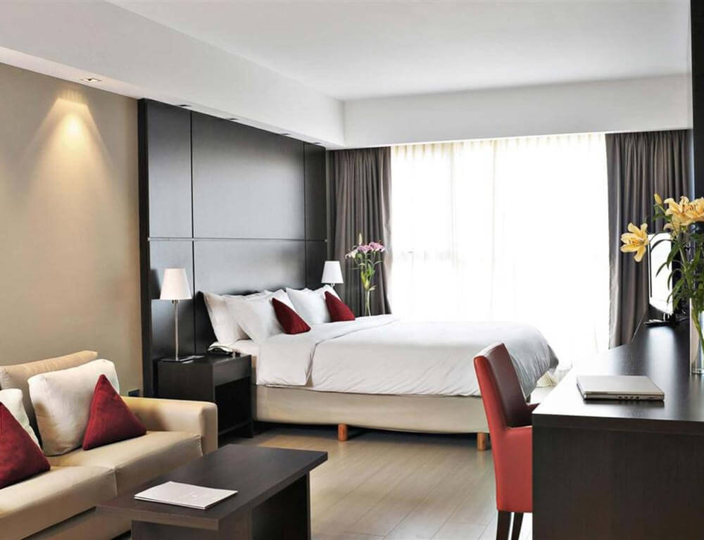 Quarto do hotel HTL City Baires, com cama de casal, sofá, TV, mesa com cadeiras e janela grande.