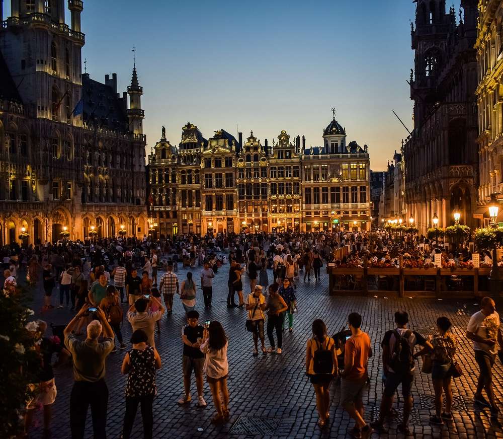 A Grand Place à noite, iluminada e cheia de pessoas caminhando e tirando fotos.