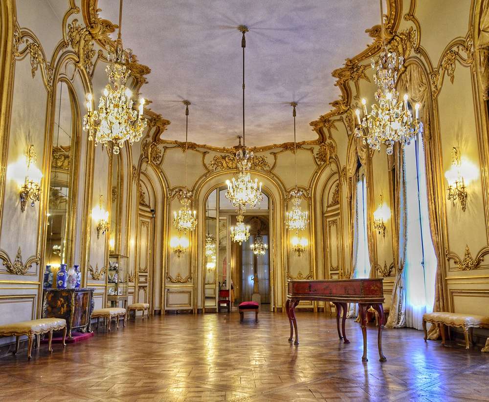 O Salão de Baile do Museu Nacional de Arte Decorativa, com arquitetura neoclássica, lustres de vidro, grandes janelas e um piano de madeira.