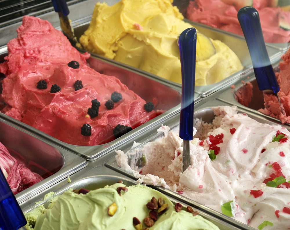 Sorvetes de diferentes cores e sabores dentro de expositor de metal.