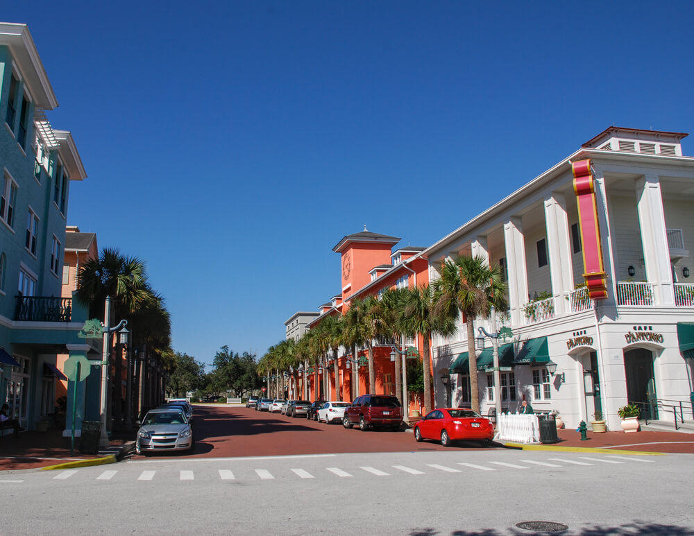 Rua do bairro Celebration, na Florida, durante o dia, com carros estácionados e prédios de arquitetura charmosa.
