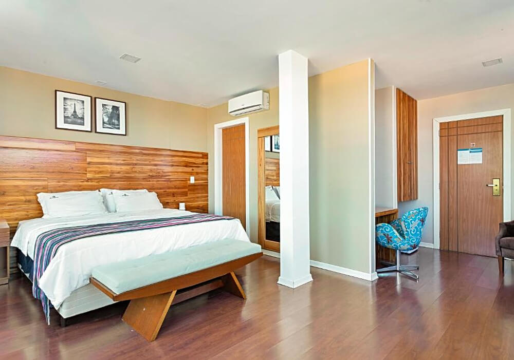 Quarto do Hotel Petrópolis Inn, com cama de casal e detalhes de madeira.