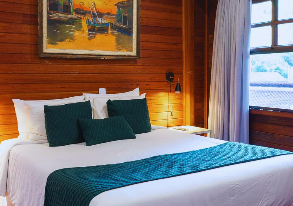 Quarto do hotel kastel Pedra Bonita com cama de casal e paredes de madeira.