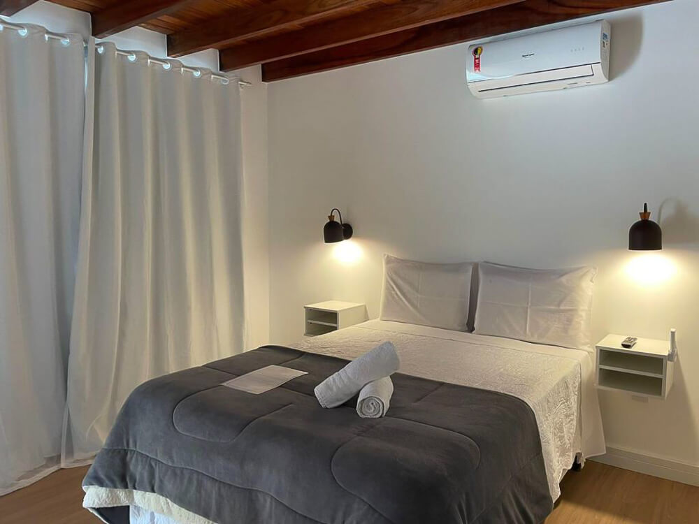 Quarto da Pousada Cozy House, com cama de casal e detalhes em tons de cinza.