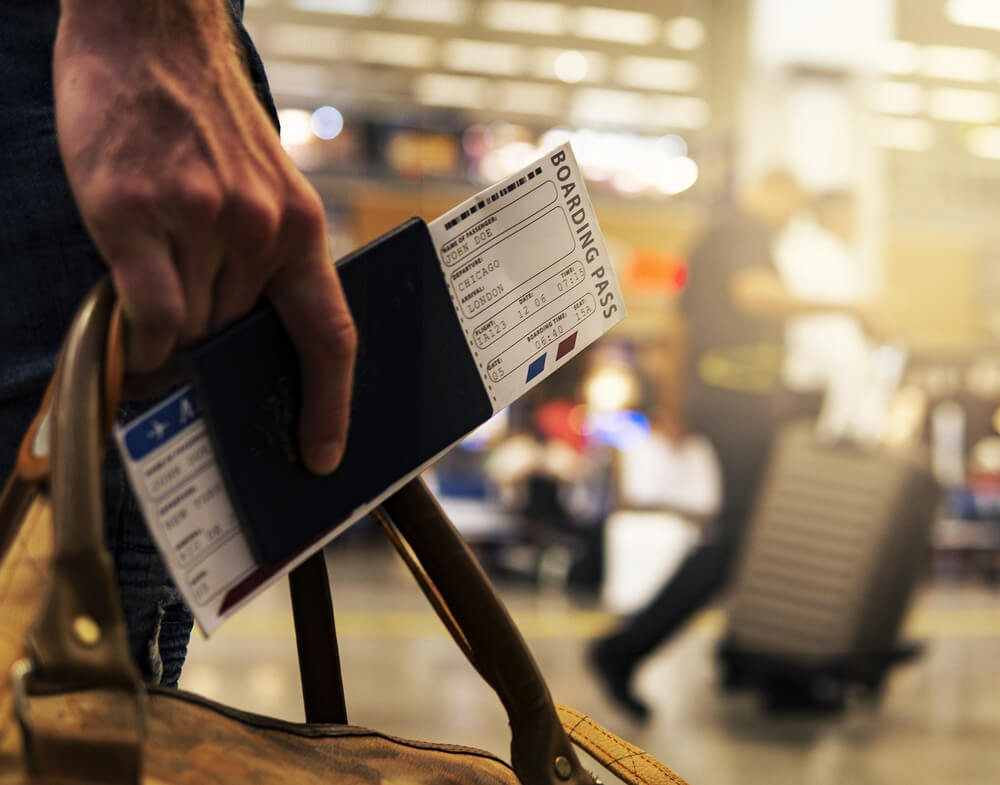 Em um aeroporto, uma pessoa segura seu passaporte, cartão de embarque e a bagagem em uma só mão.