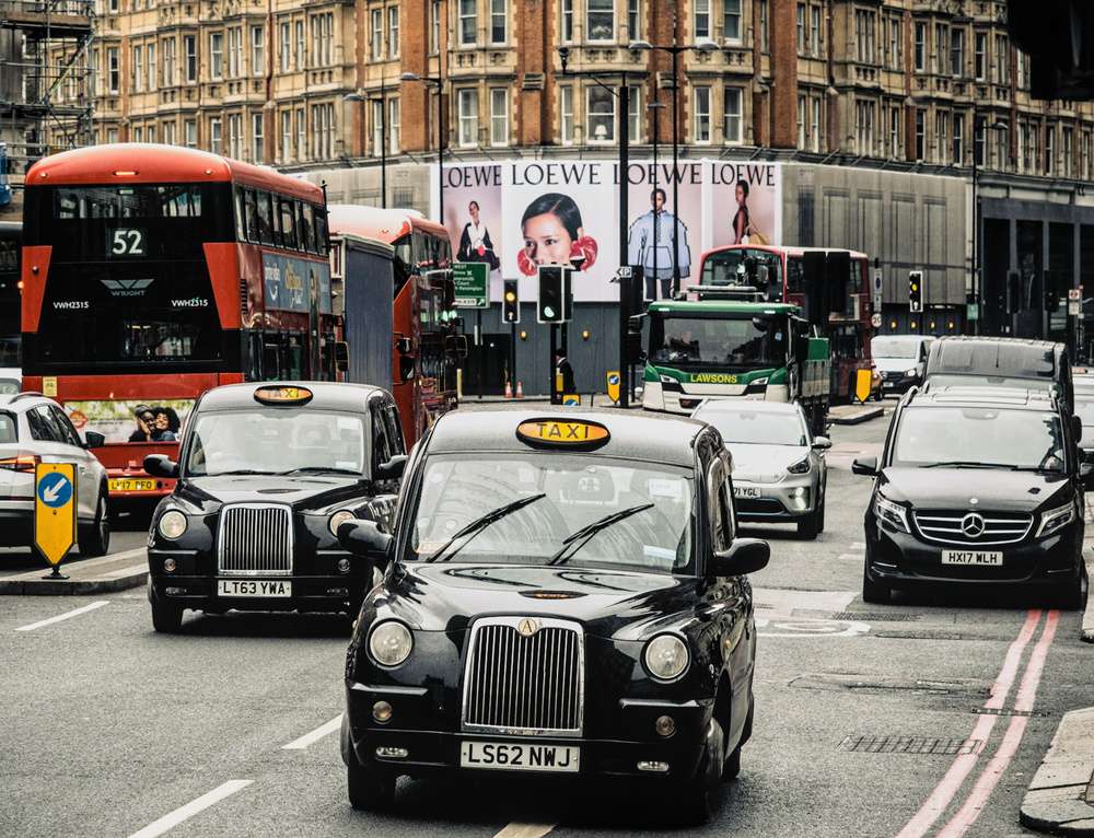 Rua de Londres com táxis pretos, carros e ônibus, vista durante o dia.
