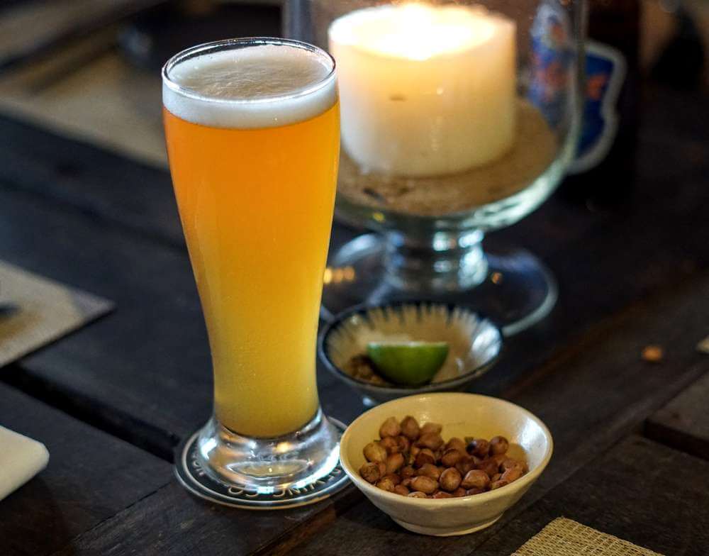 Um copo de cerveja ao lado de potinhos com amendoim e limão.