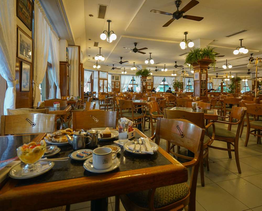 O interior do Café La Biela, com muitas mesas e cadeiras em um ambiente aconchegante.