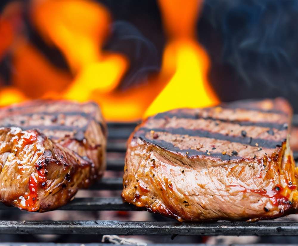Carne grelhada na grelha, com chamas ao fundo.