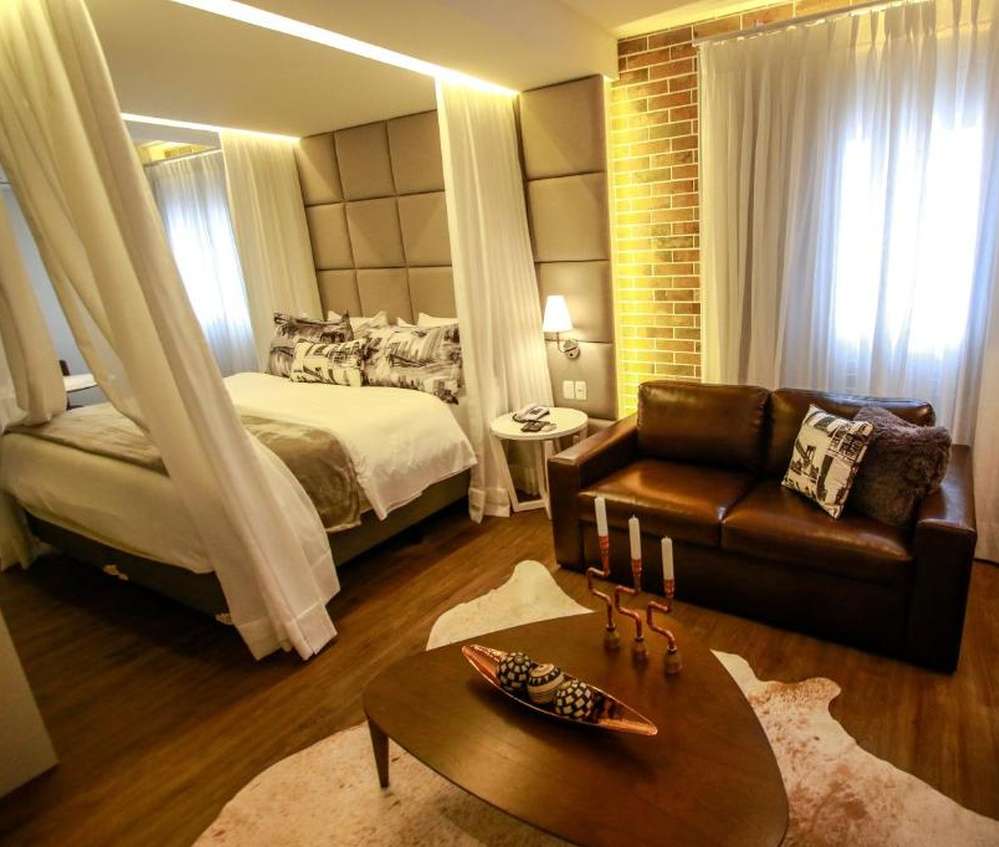 Quarto luxuoso do Hotel Cercano, com cama de dossel, sofá de couro e decoração elegante.