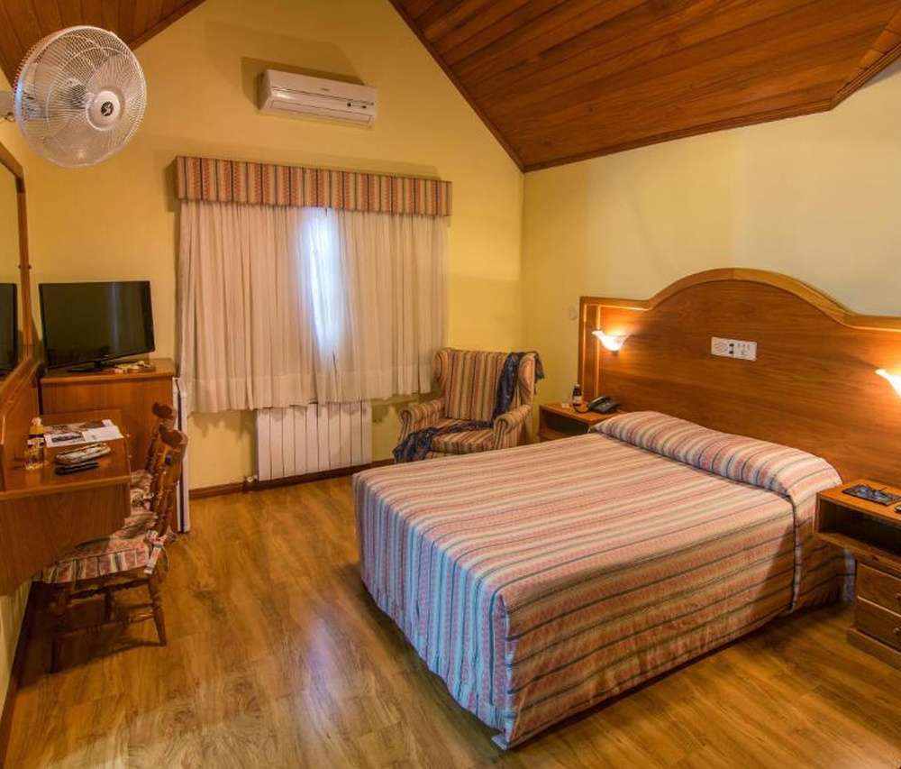 Quarto rústico do Hotel Sky Gramado, com cama de casal, penteadeira e ar-condicionado.