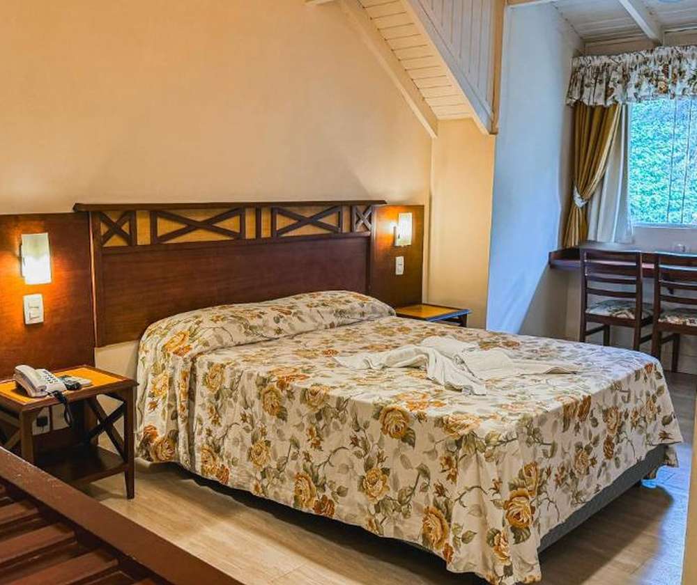 Quarto da Pousada Ald'Mama em Gramado, com cama de casal, móveis de madeira e decoração aconchegante.