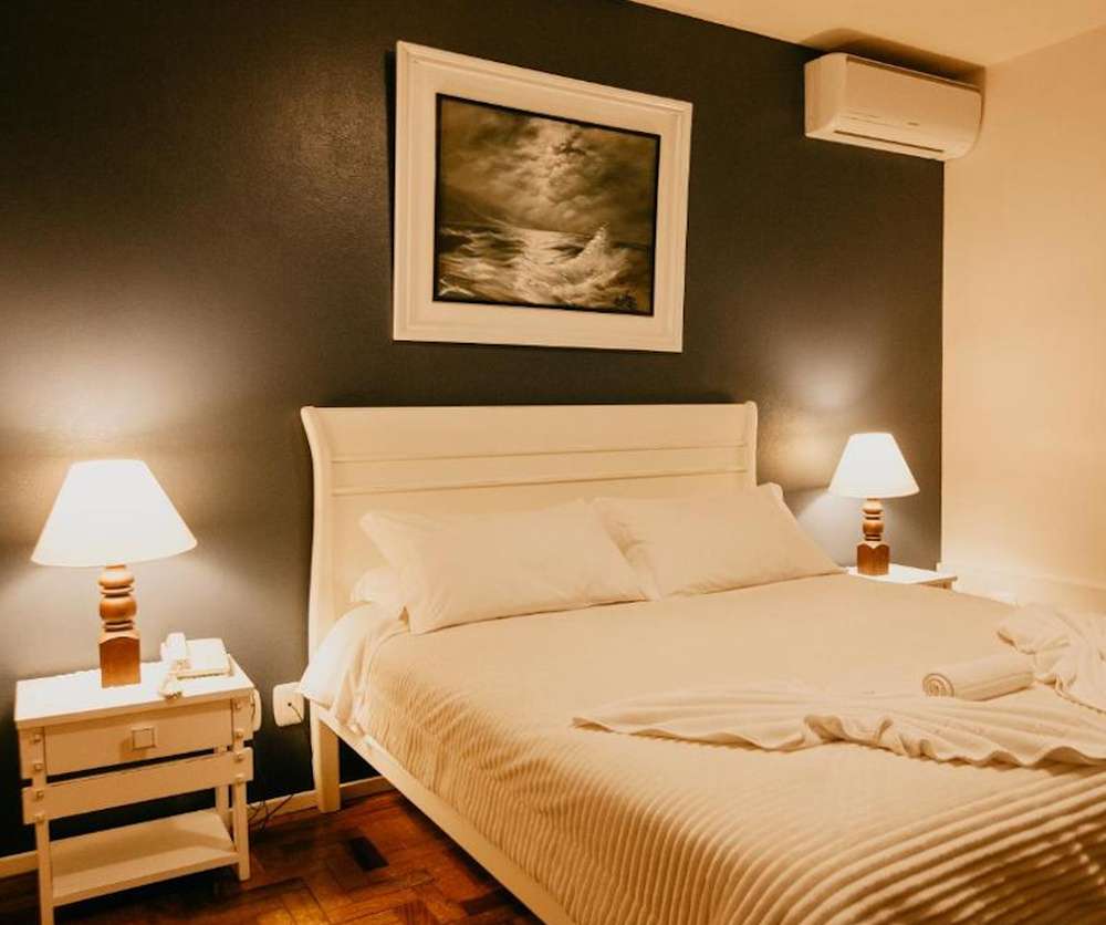 Quarto da Pousada Betânia em Gramado, com cama de casal, móveis rústico brancos e decoração elegante.