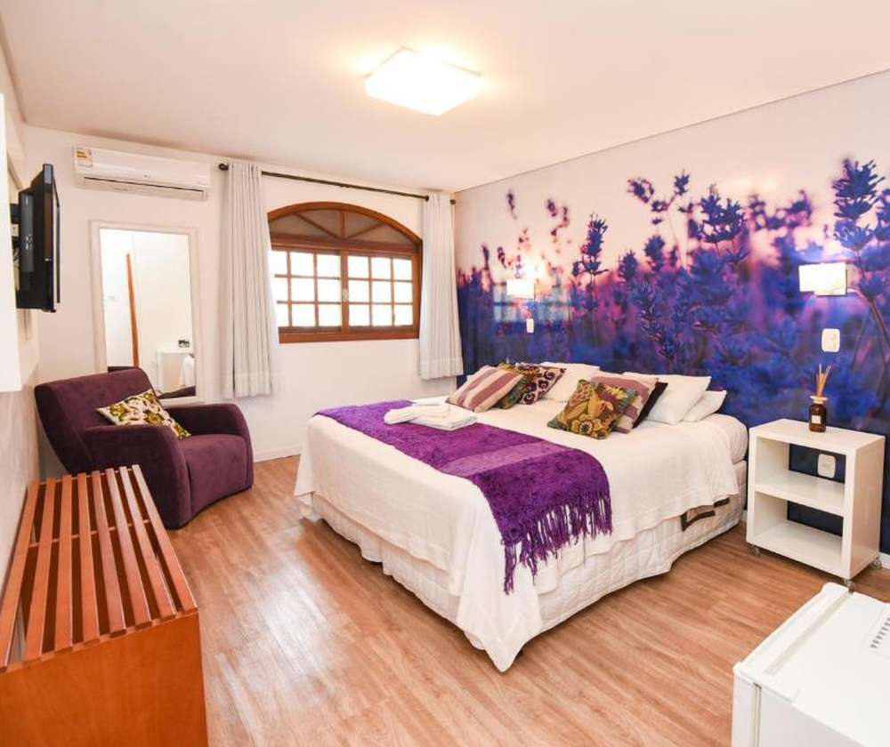 Quarto aconchegante da Pousada La Lavande, com cama de casal espaçosa e painél de lavandas na parede.