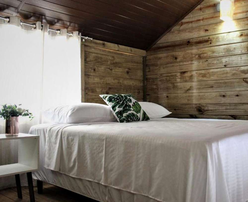 Quarto aconchegante do Garten Chalés, com paredes de madeira, cama de casal e detalhes floridos.