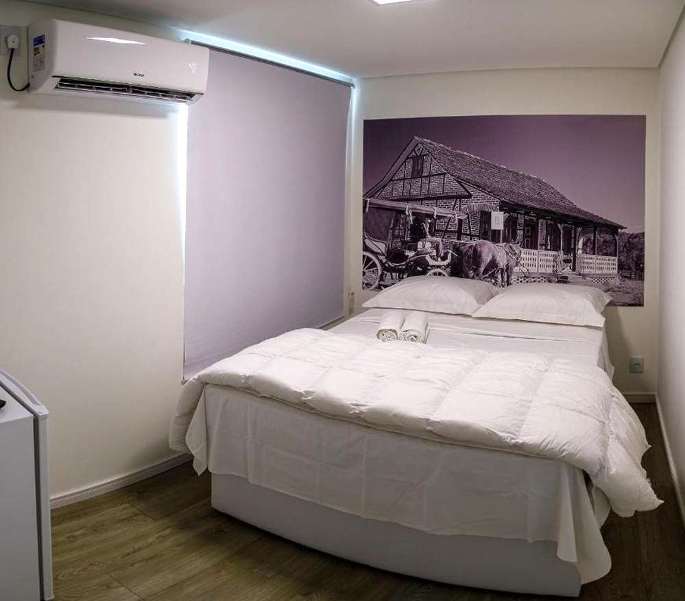 Quarto simples do Suítes Container, com cama de casal e quadro na parede com temática germânica.