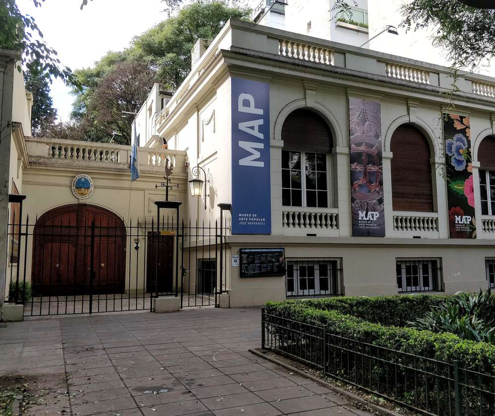 O prédio do Museo de Arte Popular José Hernández, com paredes amarelas claras, janelas arqueadas e faixas.