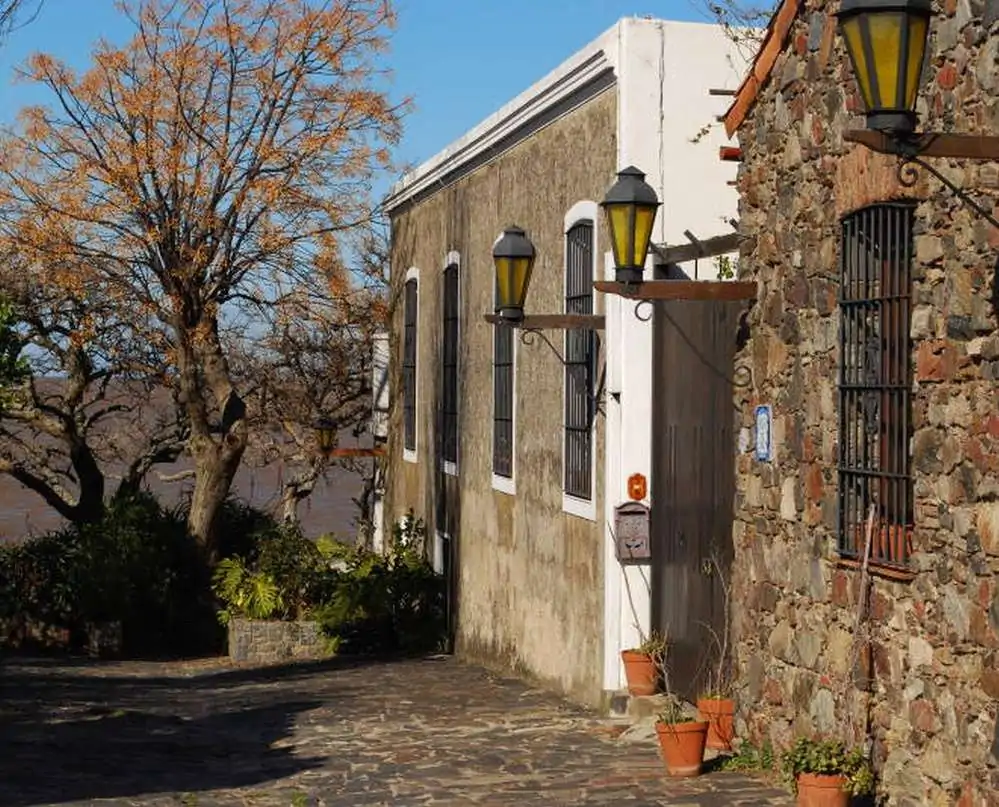 Rua do Bairro Historico de Colonia del Sacramento, com casas antigas de pedra e vegetação ao fundo.