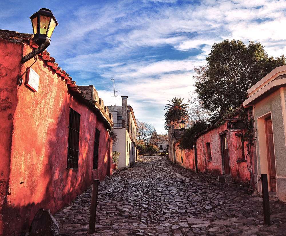 A Calle de los Suspiros, uma rua de paralelepípedos em Colonia del Sacramento, com casas coloridas e árvores ao fundo, em um dia ensolarado.