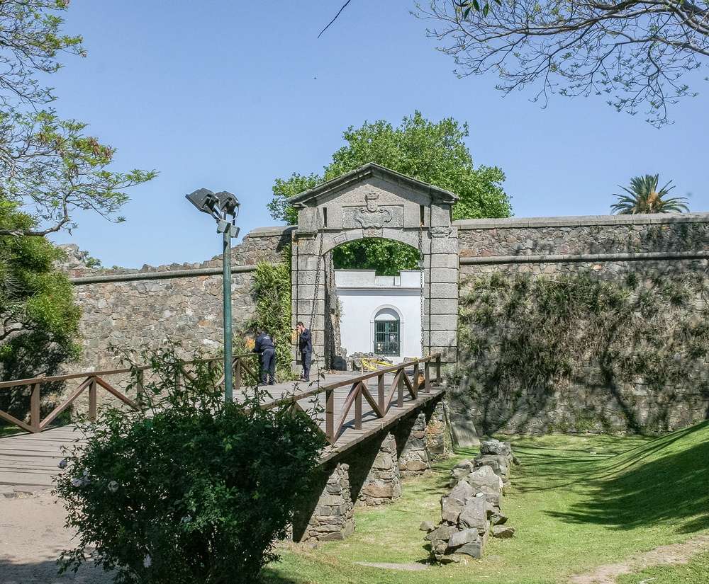 Entrada histórica da Puerta de la Ciudadela em Colonia del Sacramento, com ponte de madeira e muralhas de pedra.