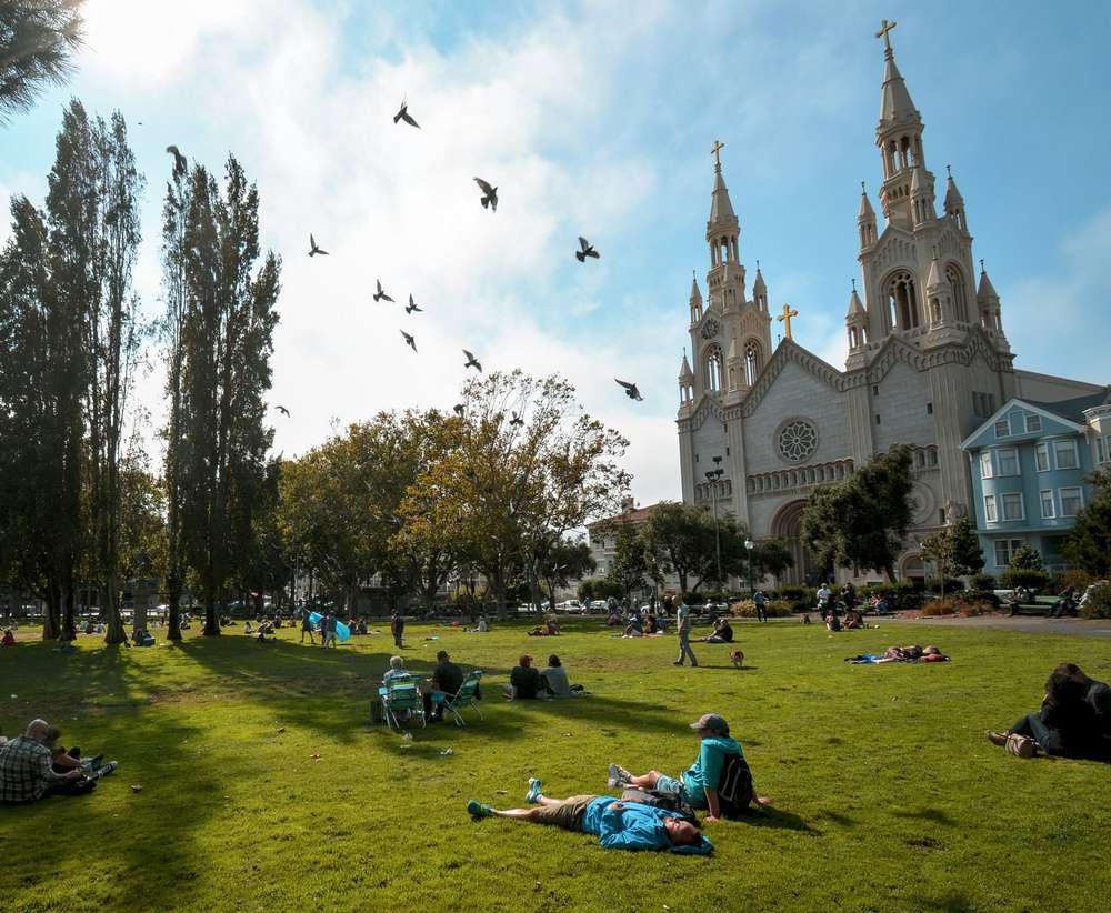 Pessoas relaxam em um gramado no Washington Square Park, em North Beach, San Francisco, com a Igreja de São Pedro e São Paulo ao fundo.