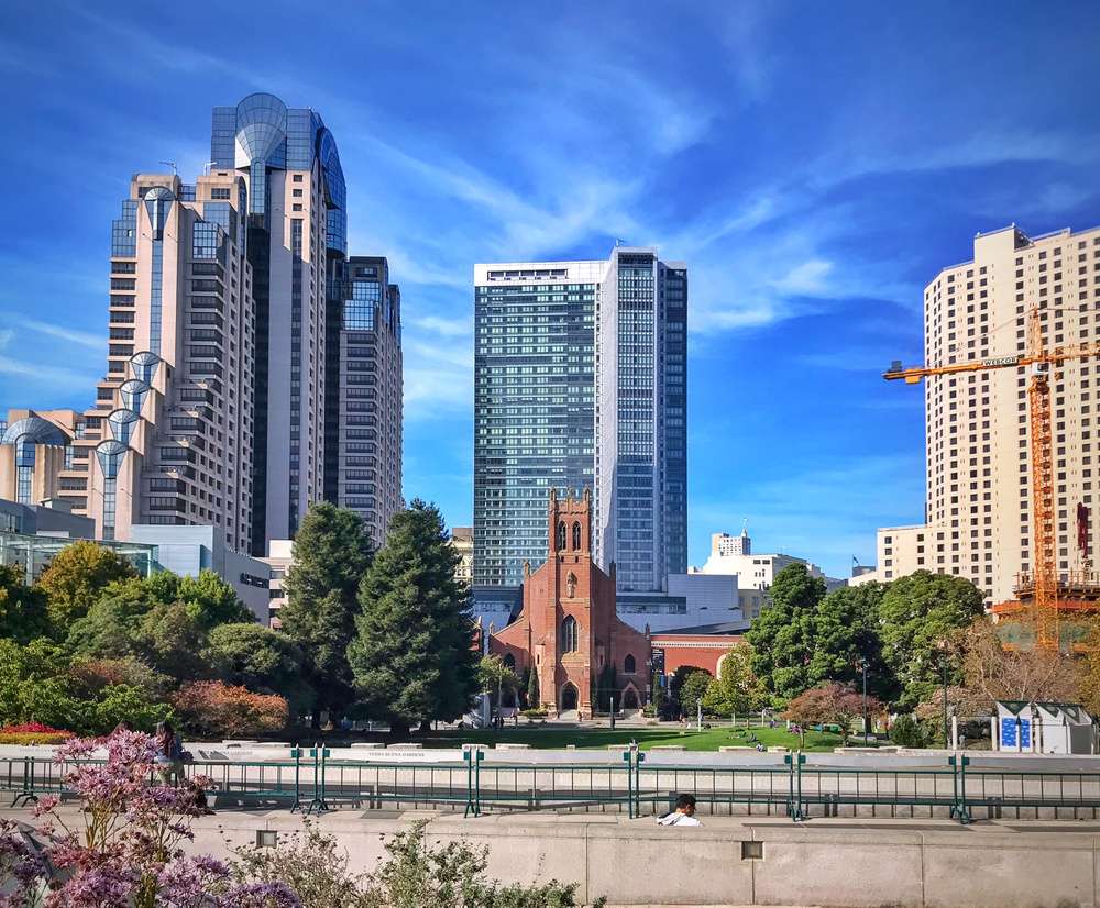 Vista do Yerba Buena Gardens, com edifícios modernos e a Igreja de St. Patrick, e árvores em primeiro plano.