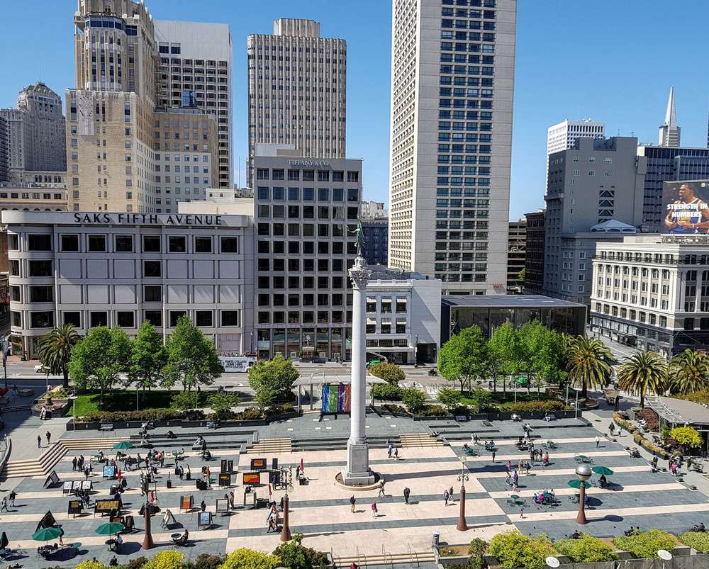 Vista da Union Square em San Francisco, com arranha-céus ao fundo e uma praça movimentada com pedestres e áreas verdes.