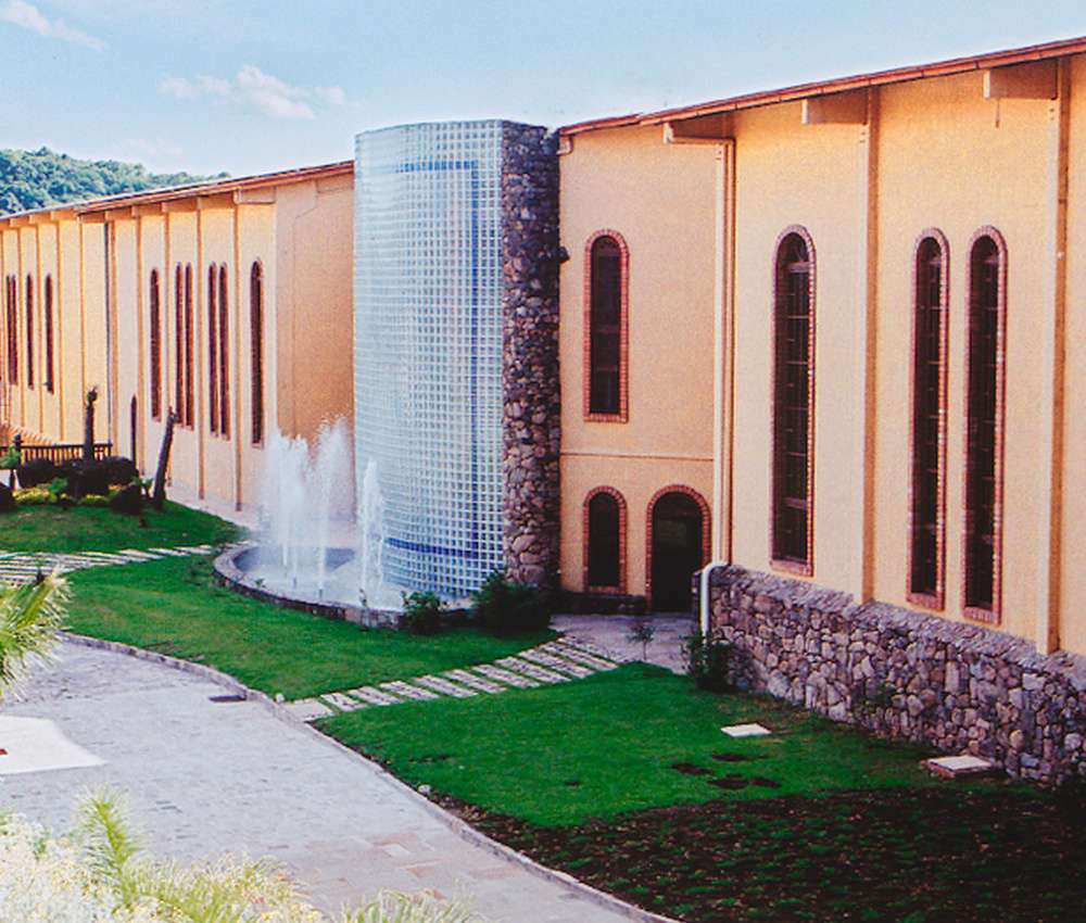 A fachada da Vinícola Casa Valduga, com paredes em tom terroso, janelas altas e um jardim bem cuidado com fonte d'água.