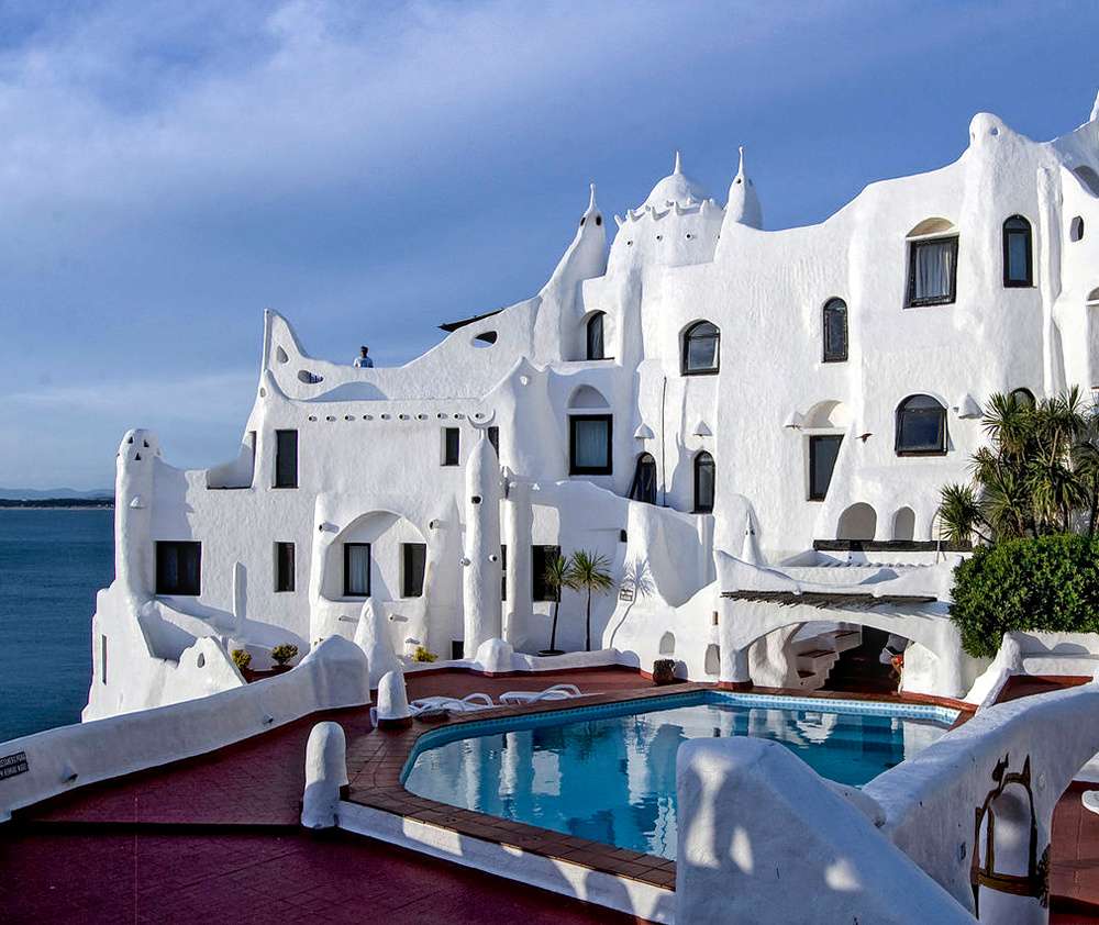 A estrutura Casapueblo, no litoral uruguaio, com uma arquitetura única branca ao lado de uma piscina com vista para o mar.