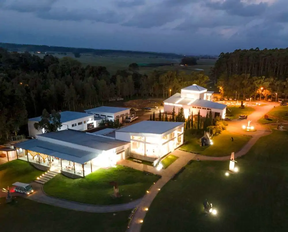 Vista aérea da Fundación Pablo Atchugarry durante a noite, destacando prédios com formatos modernos e iluminados, dentro de uma área muito arborizada.
