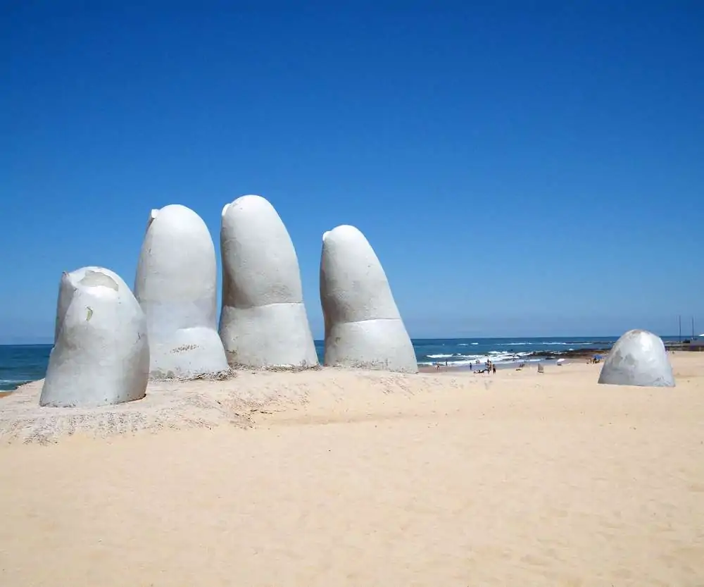 A escultura La Mano na areia da Playa Brava, em um dia de céu azul e sol forte.
