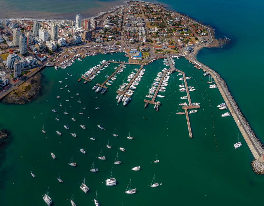 Vista aérea do porto de Punta del Este, Uruguai, mostrando barcos ancorados e uma área urbana ao lado.