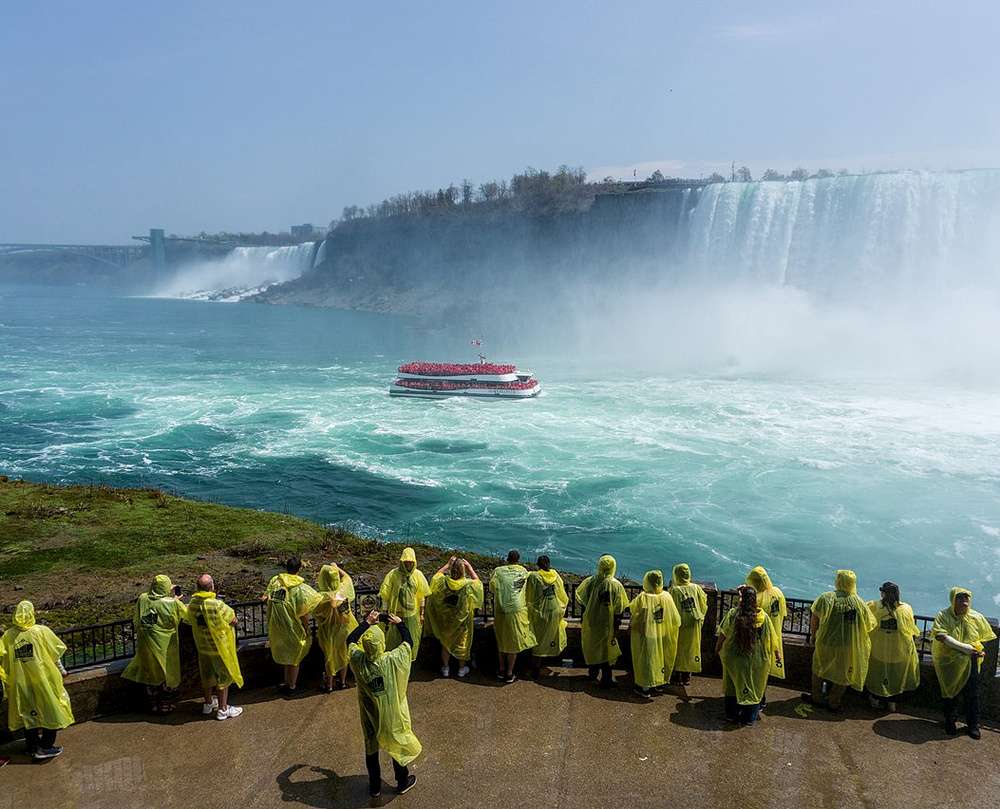 Turistas vestindo capas de chuva amarelas observam as imponentes Cataratas do Niágara a partir de um mirante.