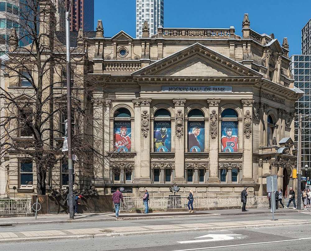 A fachada do Hockey Hall of Fame em Toronto, um prédio clássico adornado com banners de lendas do hóquei, em um dia claro.