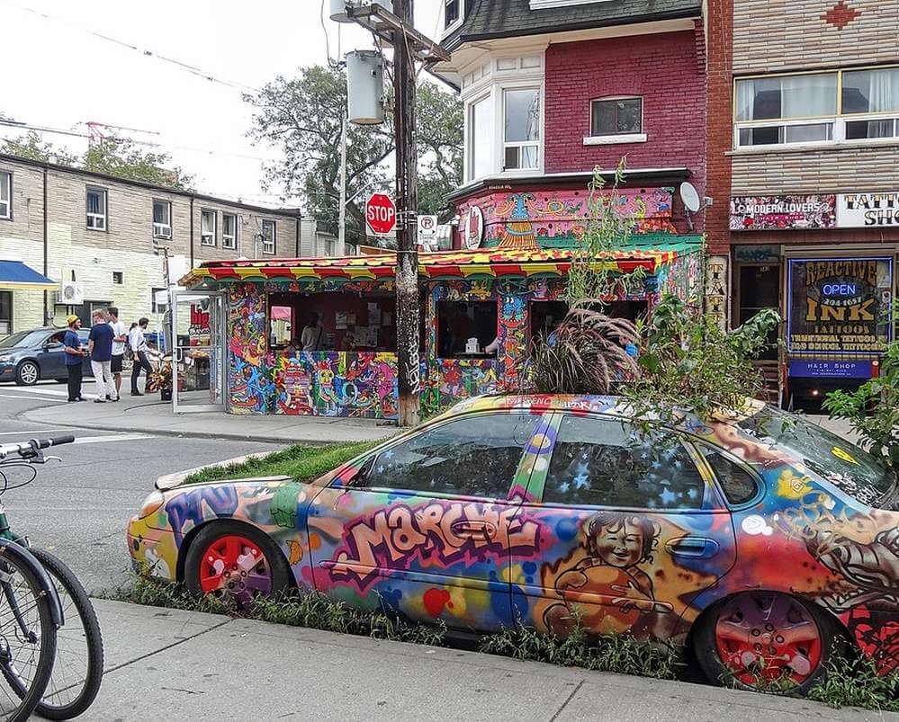 Uma das ruas do Kensington Street durante o dia, com um carro cheio de arte grafitti e plantas.